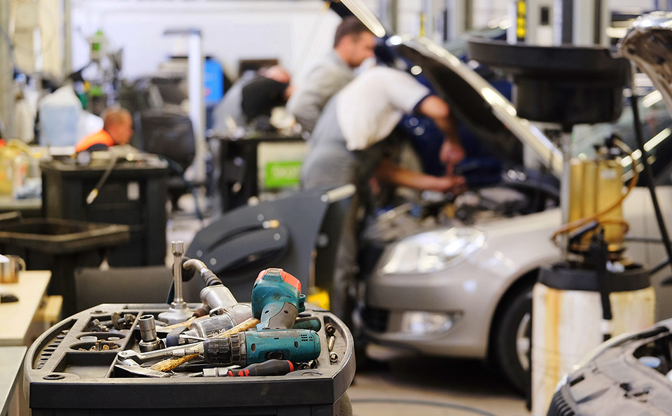 Auto repair shop with mechanics and a tool cart in the foreground.